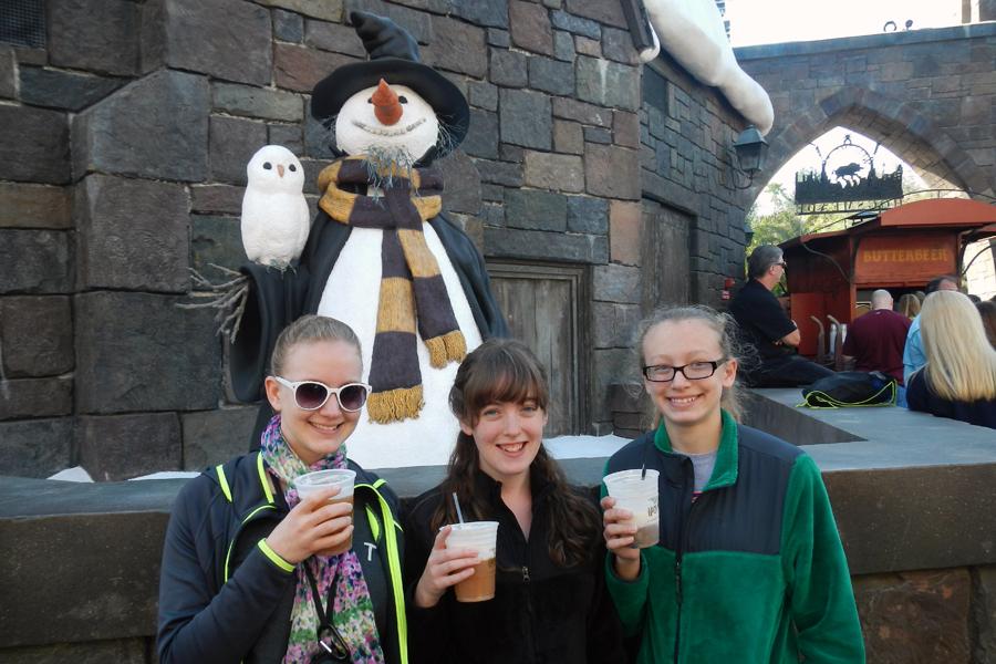 Tasha Brown, Breanna Bassett and Josie Brown sip on butterbeer in the Wizarding World of Harry Potter while a wizard-like snowman looks on.