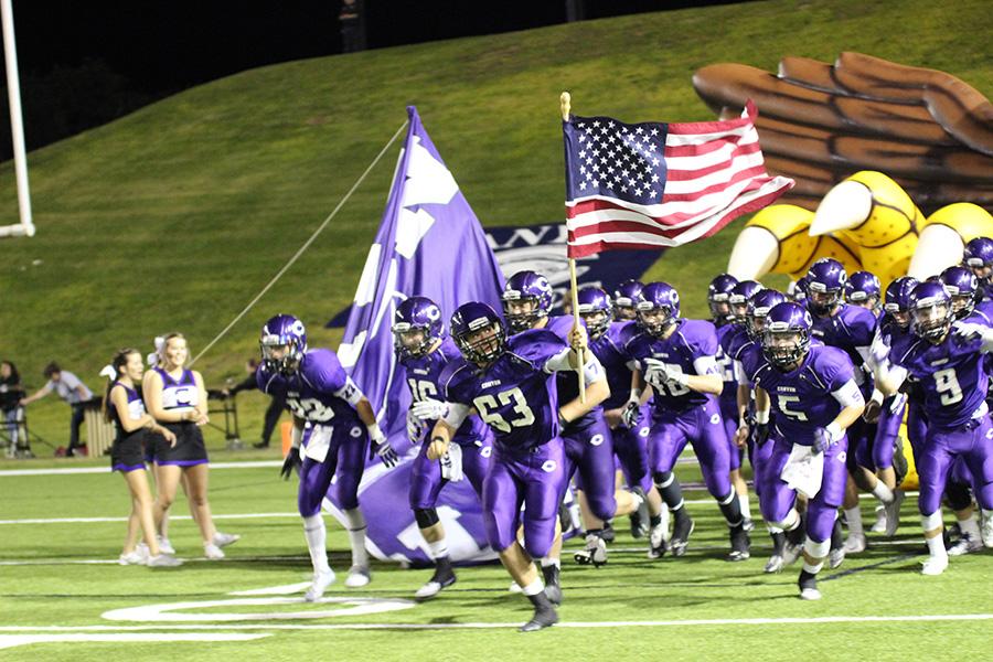 The Canyon football team bursts out of the Eagle tunnel, led by senior Clint Halencak with the American flag.