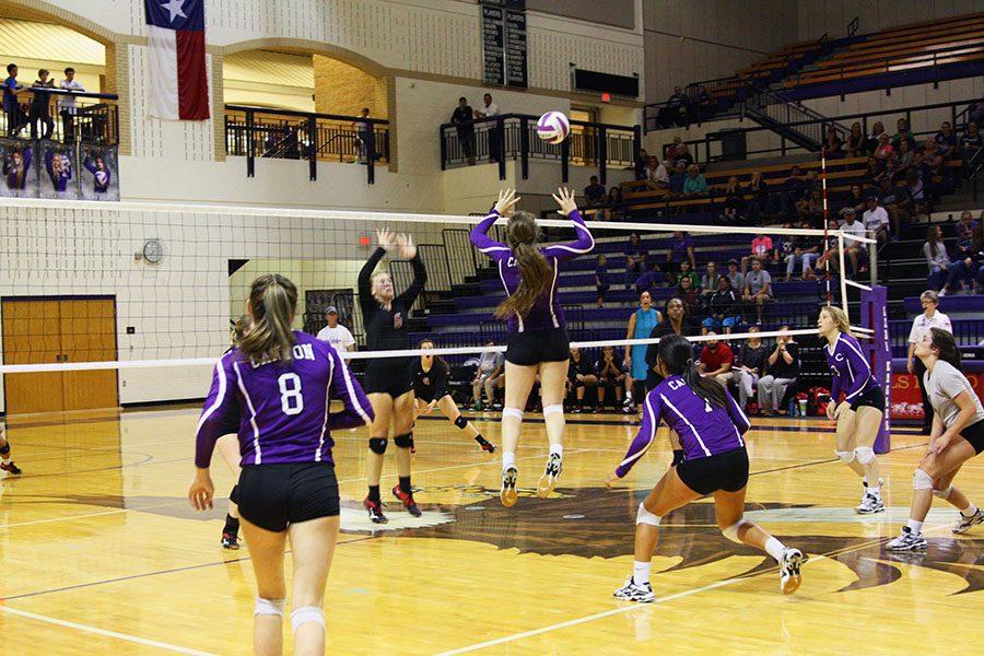 Junior Kennedy Wood jumps to set the ball over the net while her team prepares to cover her.