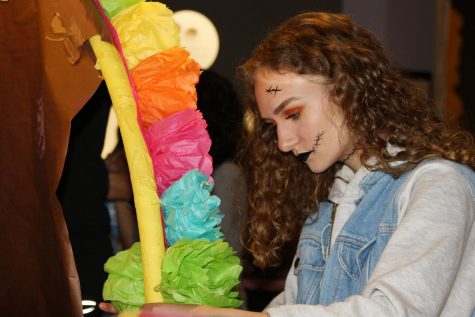 Junior and Spanish IV student Madeline Shadduck glues flowers she made in class on the arch of the ofrenda while setting up at the museum.